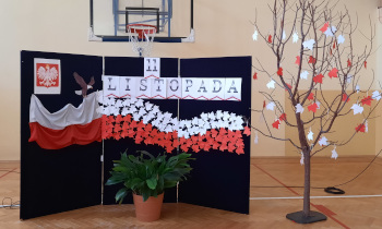 Sala gimnastyczna. Na ciemnej ściance napis 11 listopada. Godło i&nbsp;flaga Polski. Obok drzewko z&nbsp;białymi i&nbsp;czerwonymi liśćmi.