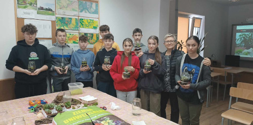 uczniowie klasy ósmej stoją i trzymają swoje prace florystyczne, wśród nich stoi również nauczycielka ZCKR, która prowadziła warsztaty.